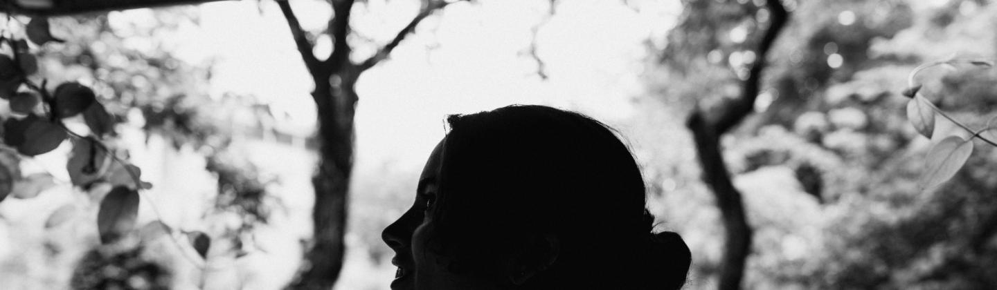 Black and white image of a young female student silhouetted in a garden