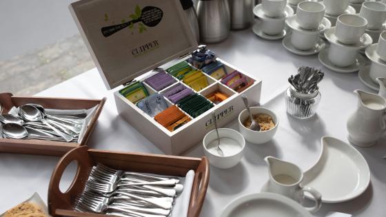Elegant catering table with white cloth, set with box of teas, silver cutlery, white coffee cups