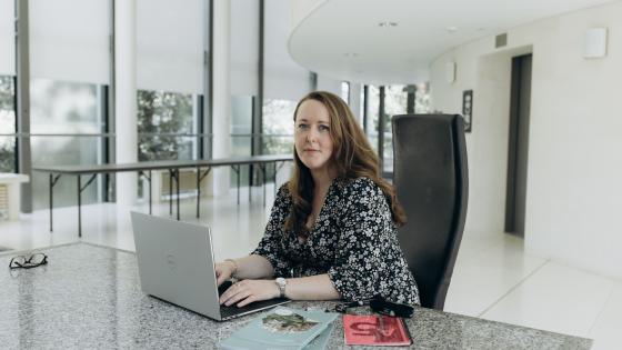 Woman at laptop at marble desk in large office space