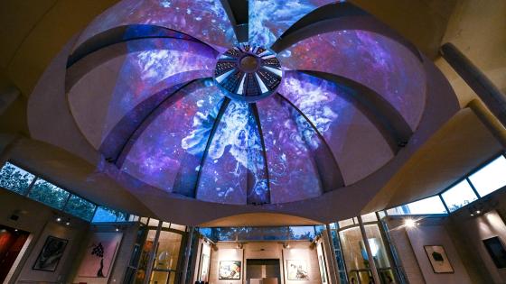 Interior shot of the Dome dining hall at Murray Edwards College, set up ready for an event.. A colourful blue and purple galaxy image has been projected onto the huge Dome ceiling.