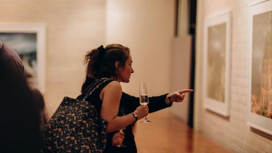 Two women admiring an artwork, holding a glass of champagne.